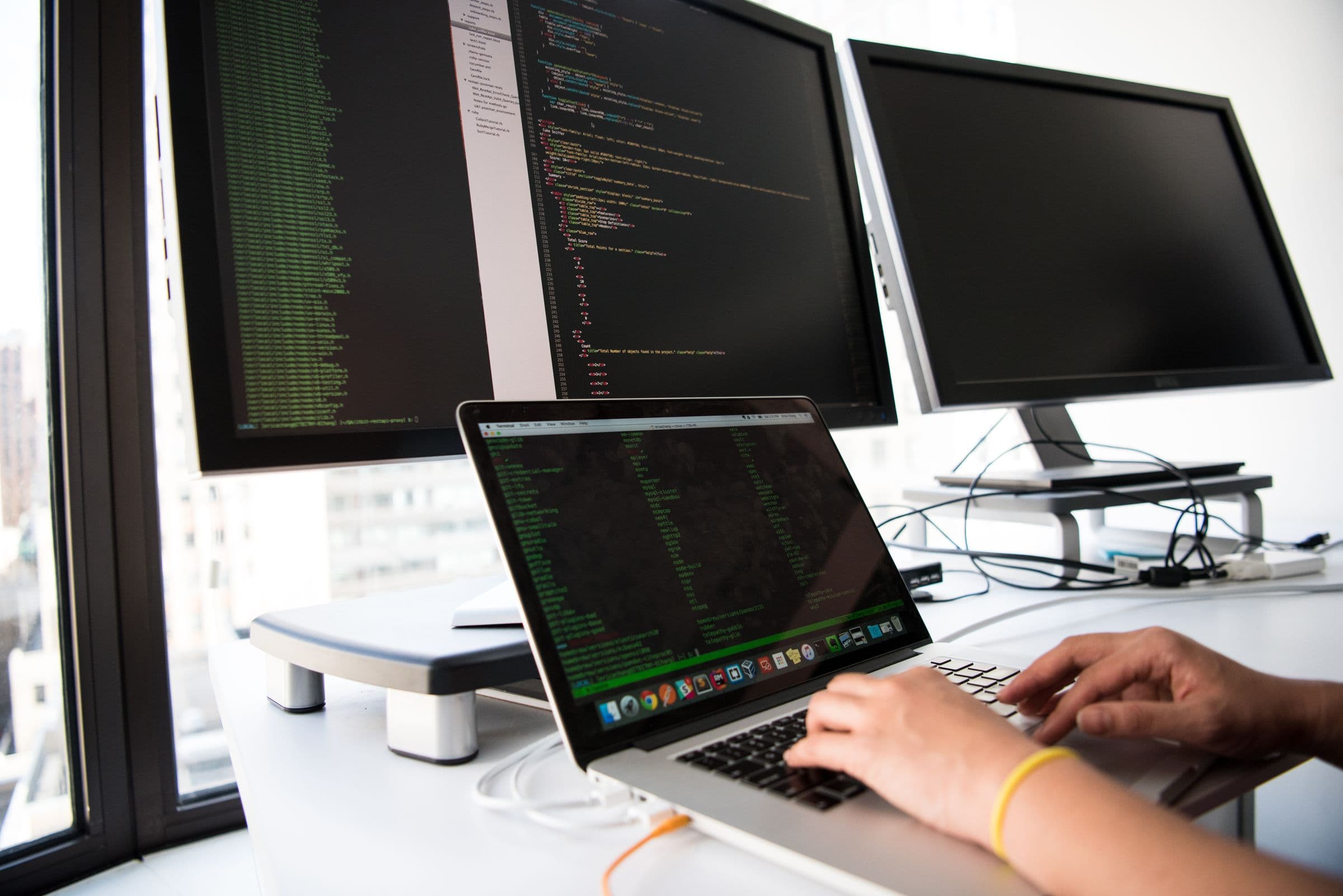 Handen op een laptop met code voor twee monitoren