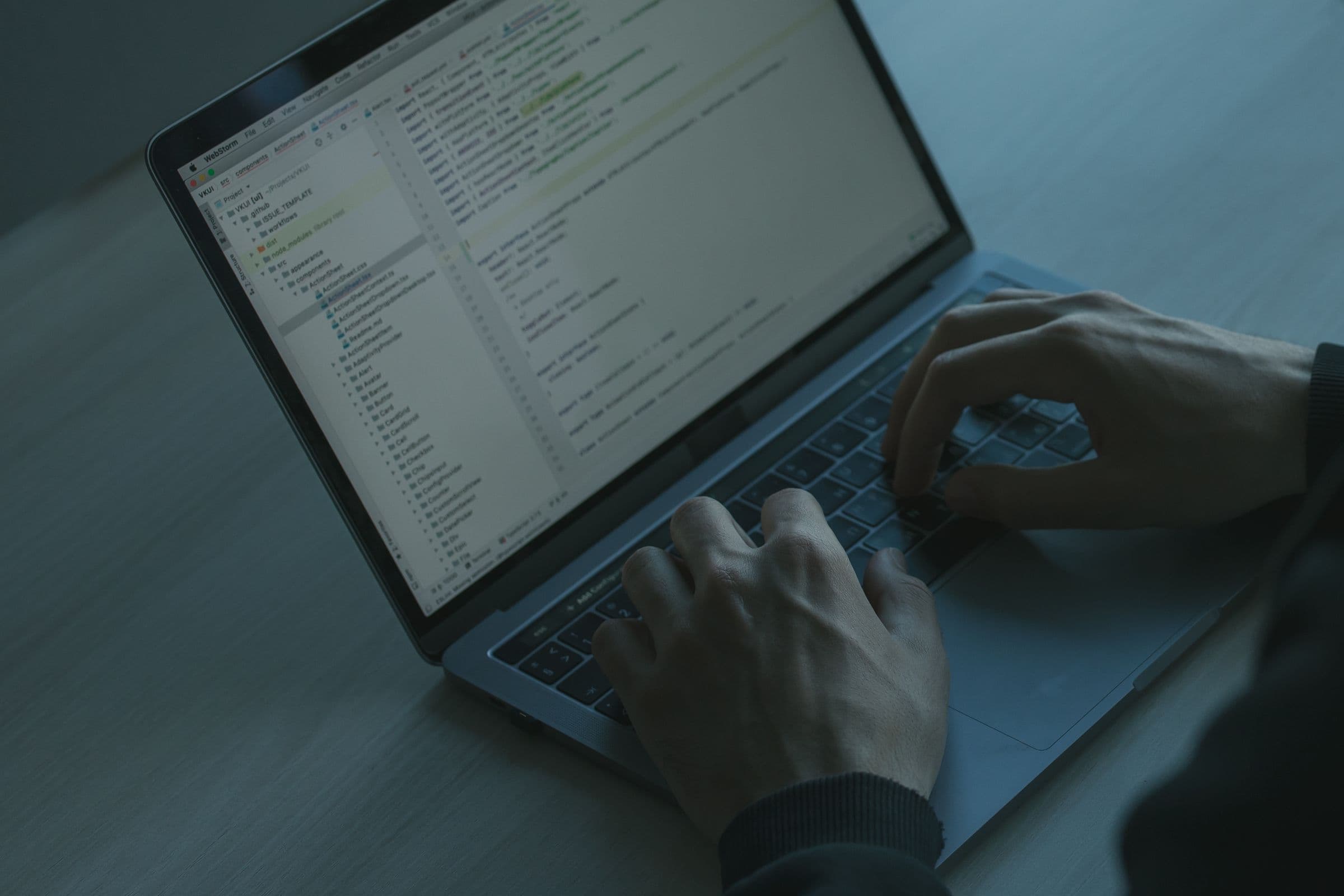 Handen op het toetsenbord van een laptop met een code-editor, in blauwig licht