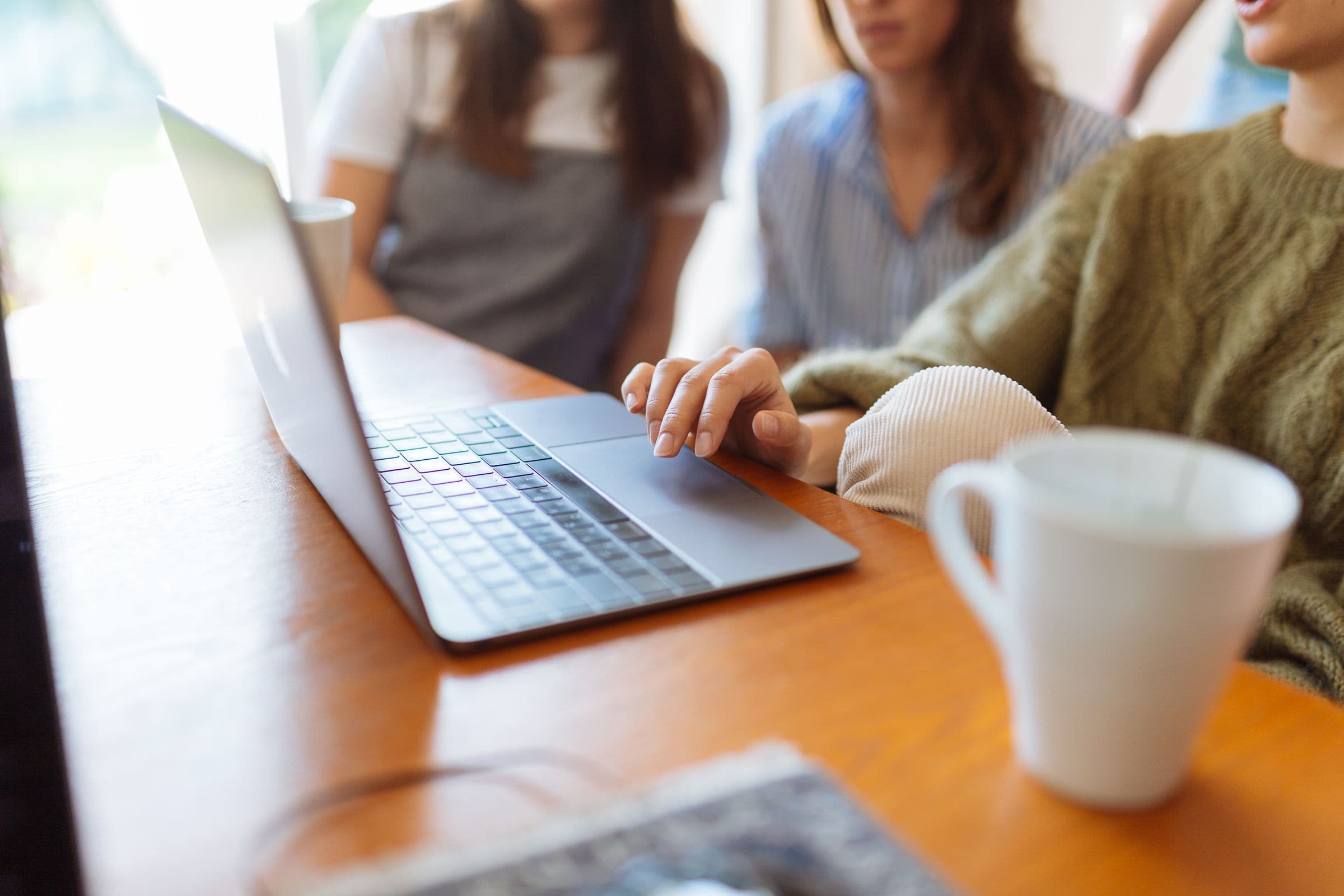 Handen op een laptop aan een tafel, met collega's onscherp op de achtergrond