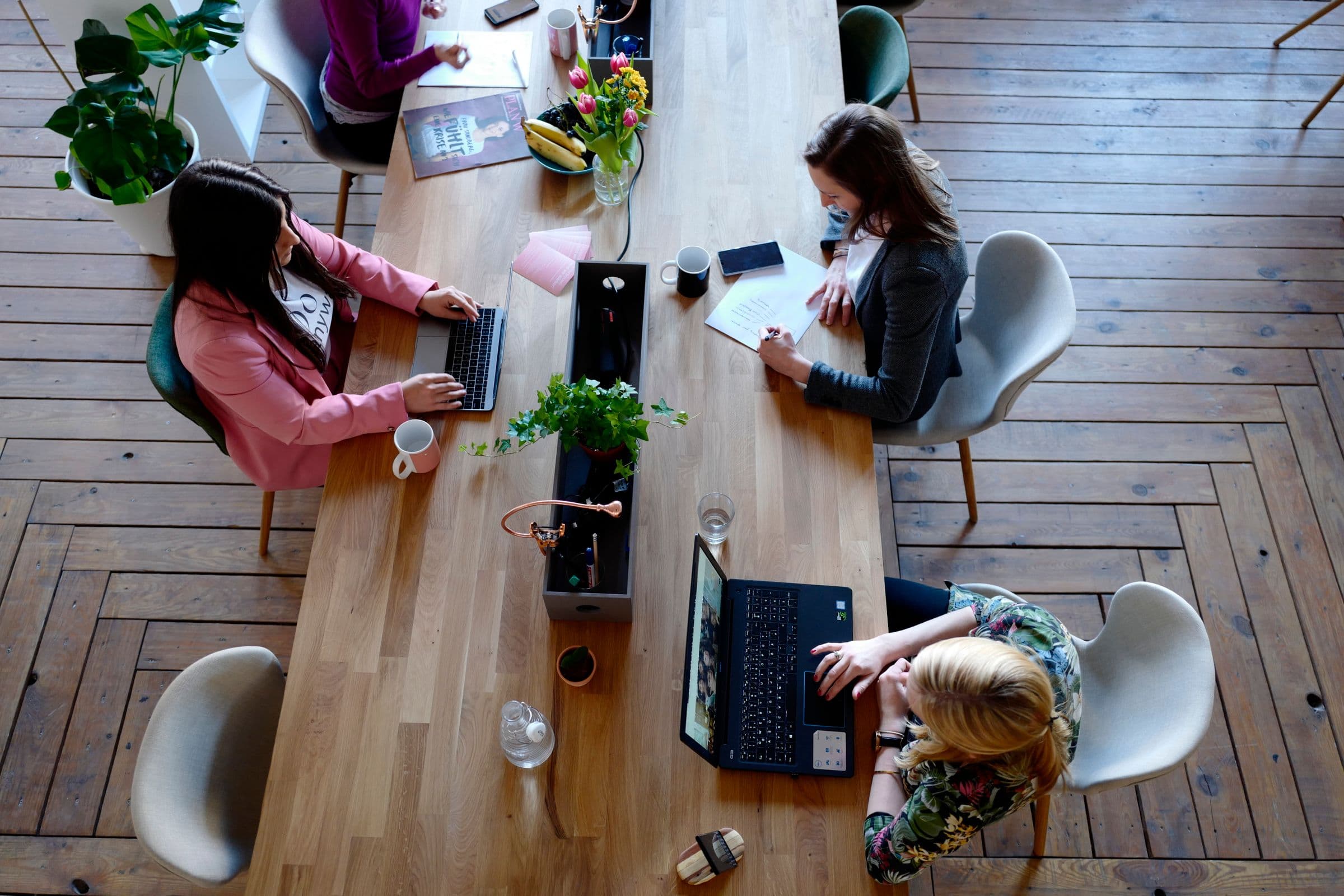 Bovenaanzicht van een lange tafel waar mensen op laptops werken