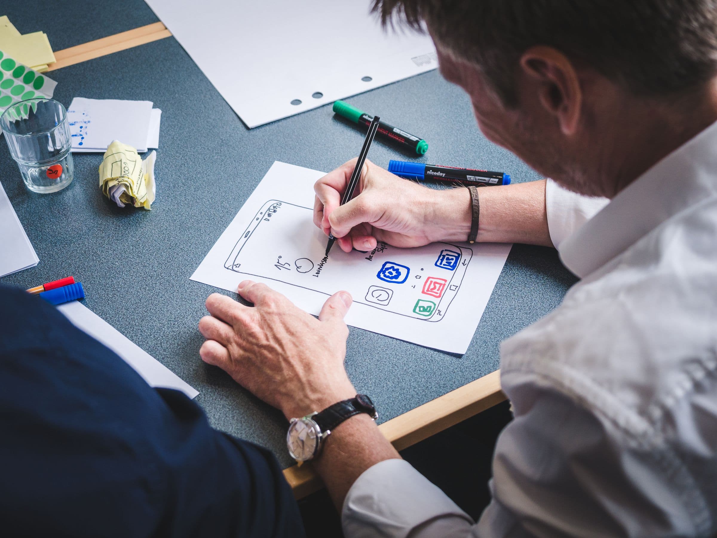 Handen die een schermontwerp op papier schetsen, met stiften op tafel